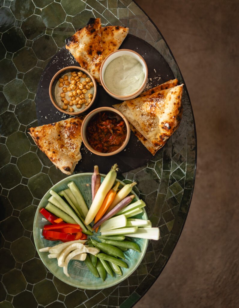 An overhead view of flatbread, three dips and fresh vegetables on a green tiled table at Florentin