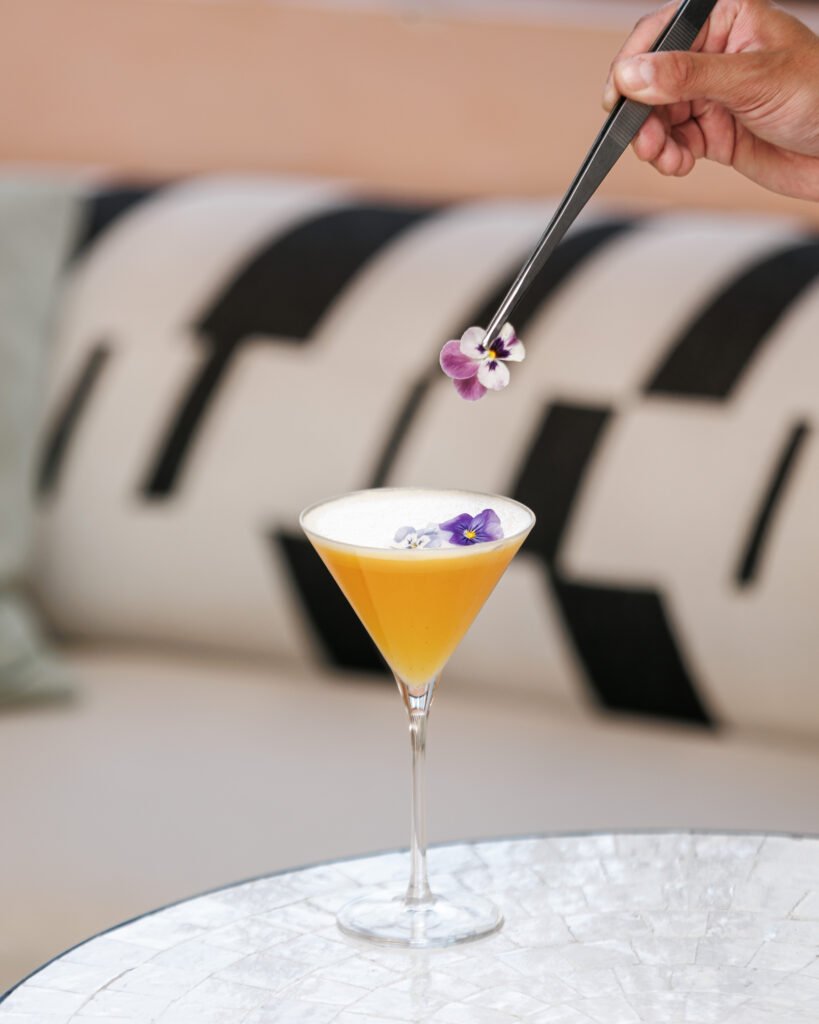 A pansy flower being placed on a golden Florentin cocktail